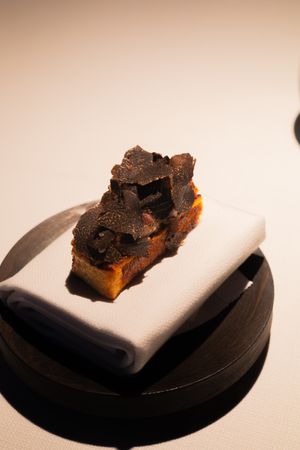 Series of dark truffles or chocolate pieces served on minimalist white plates against a neutral background.