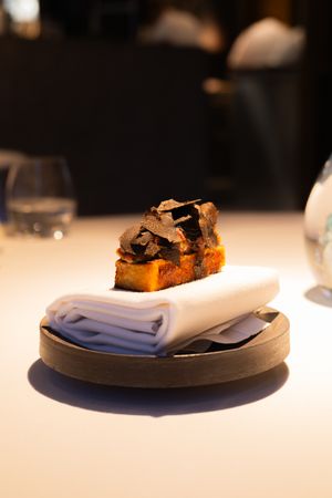 Fine dining plate presentation with dark elements on crisp white tablecloth.
