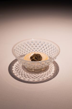 Ornate glass serving plate with decorative pattern holding a small culinary creation.