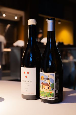 Two wine bottles displayed on a white table against a warm, dimly lit restaurant background.
