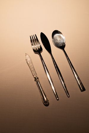 Silverware and utensils arranged diagonally with dramatic lighting and shadows on a gradient background.