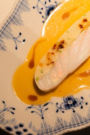 White fish fillet served with vibrant yellow sauce on decorative blue and white plate.