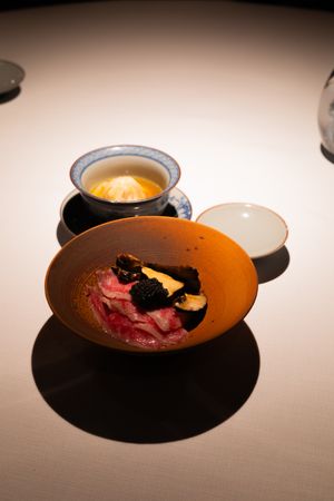 A series of orange ceramic bowls showing the progression of a plated dessert with dark garnishes and red elements.