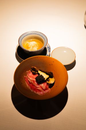 Artistic plating of orange-hued soup or sauce in dark ceramic bowls with garnishes.