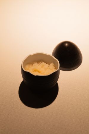 A spherical black container revealing white rice inside against a beige background.