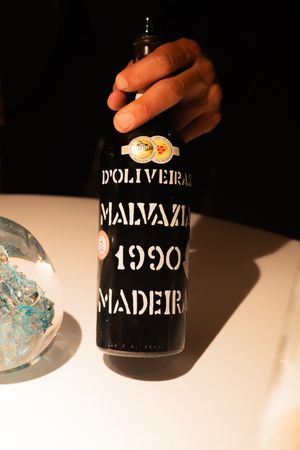 Vintage Malvazia and D'Oliveira Madeira wine bottles casting shadows on white surface.