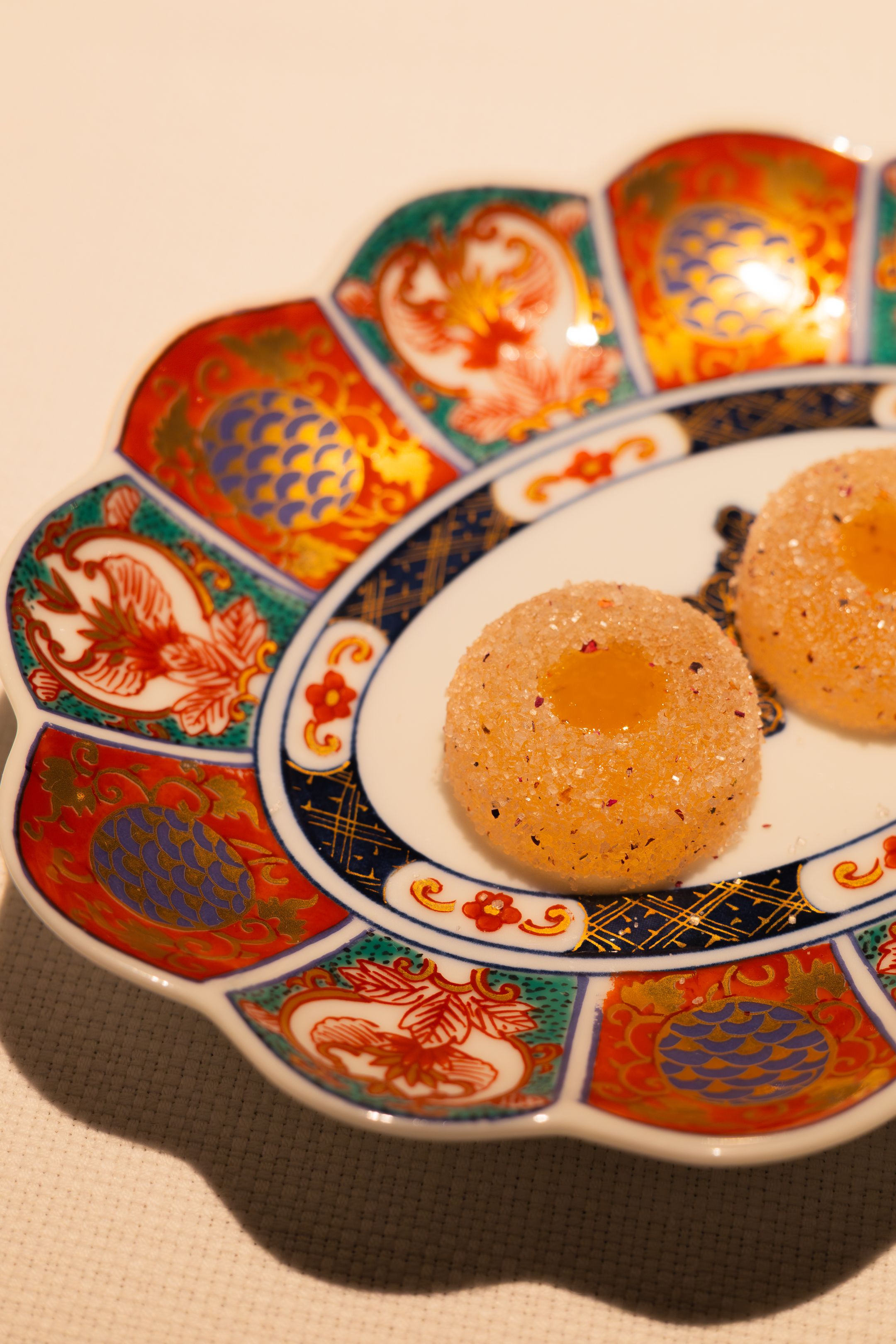 Traditional Japanese plate with colorful floral patterns holds two mochi desserts with golden centers.