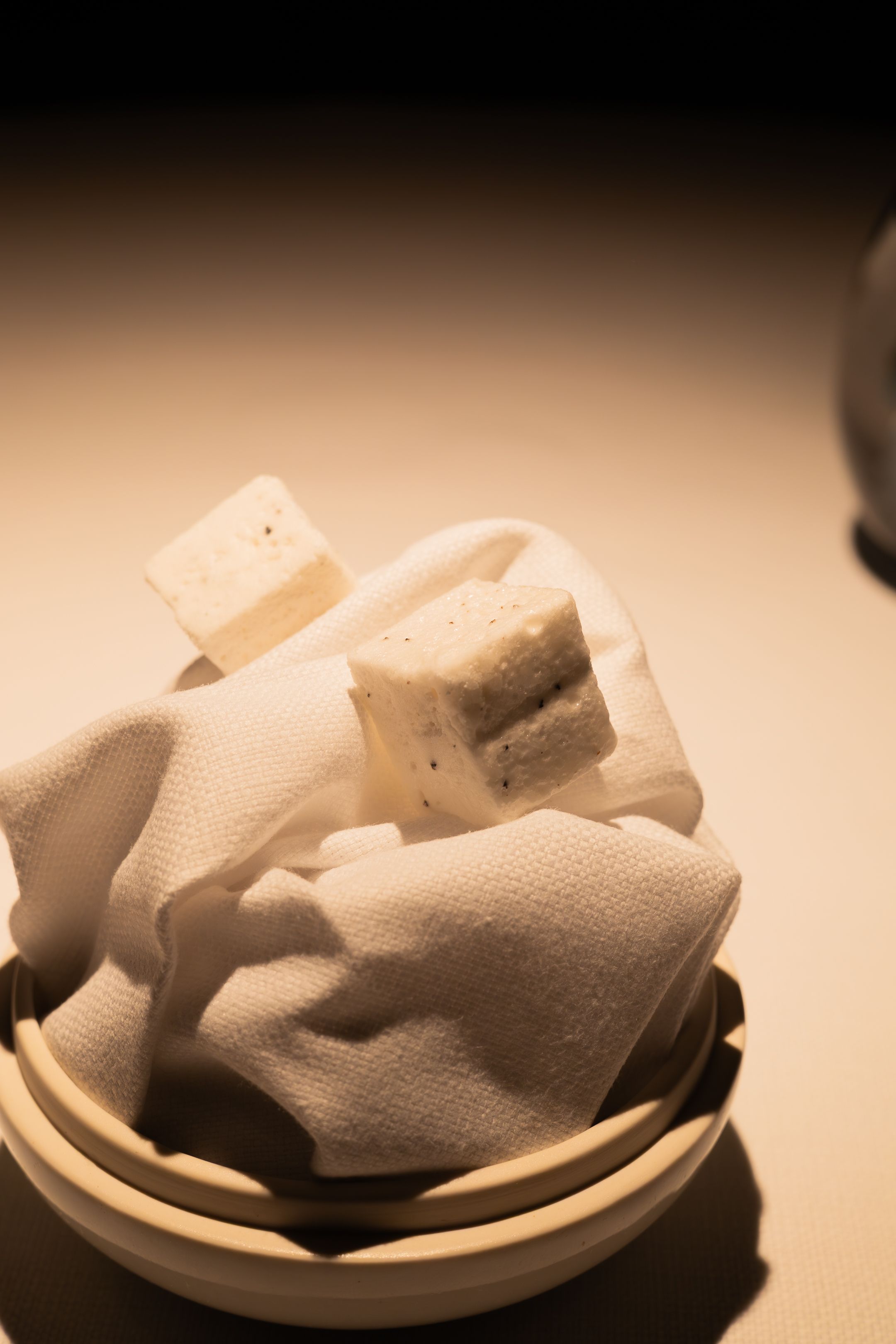 White marshmallows sit atop crumpled napkins in a small ceramic bowl under warm lighting.