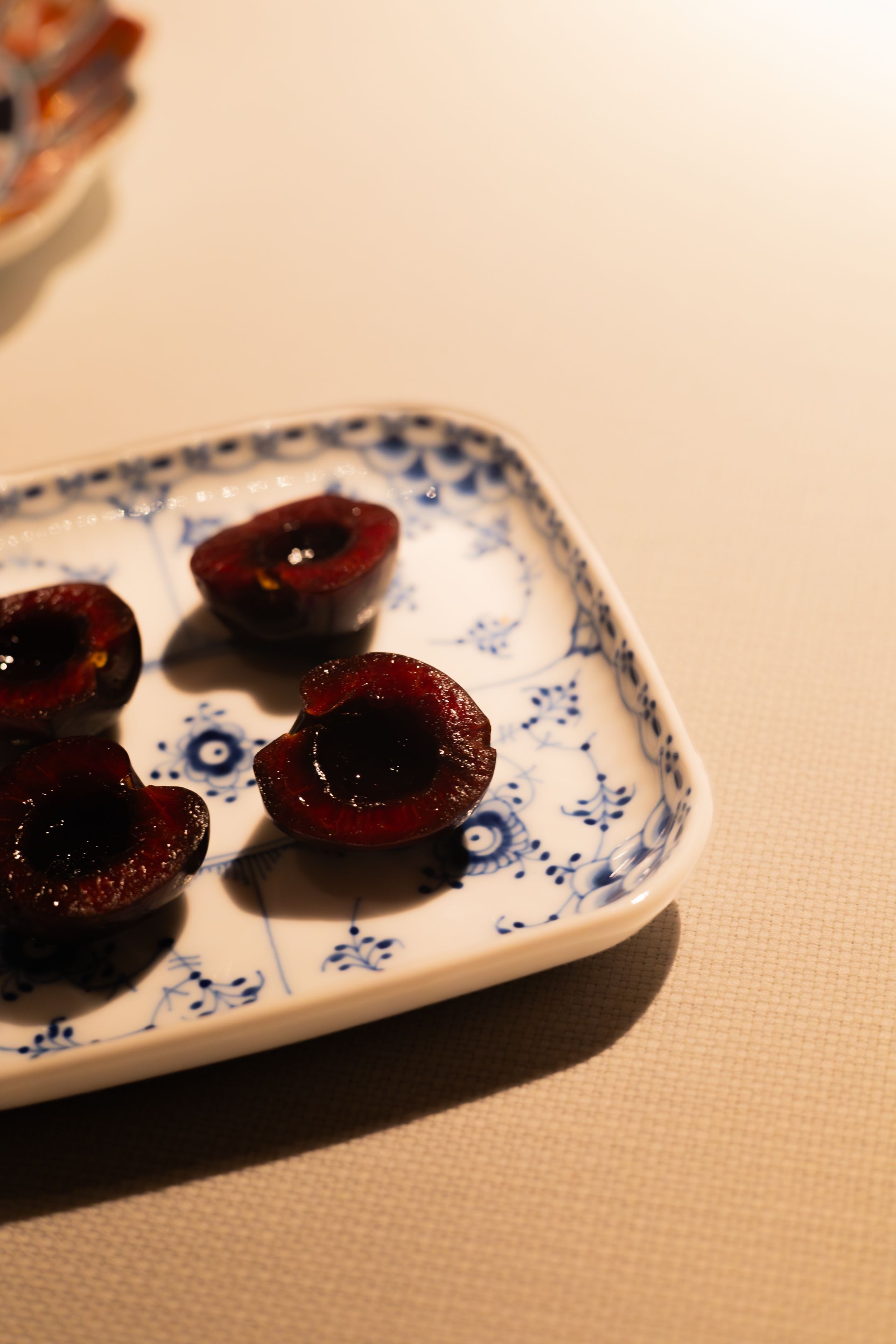 Fresh dark cherries arranged on a decorative blue and white porcelain plate against a neutral background.