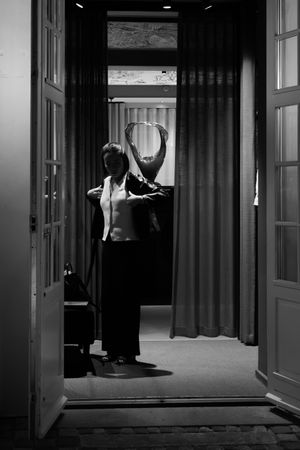 Dramatic black and white film noir style sequence showing a shadowy figure entering through doorways in a dark hallway.