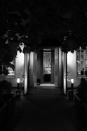 Dark hallway with illuminated doorways and windows creating a moody nighttime ambiance.