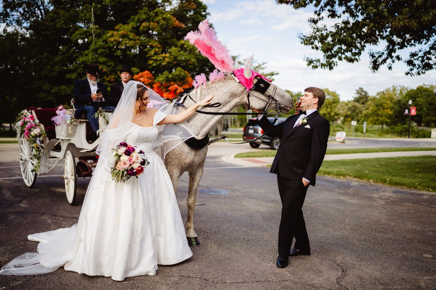 Wedding party poses with a friendly donkey in formal attire on a sunny outdoor path at a rustic venue.