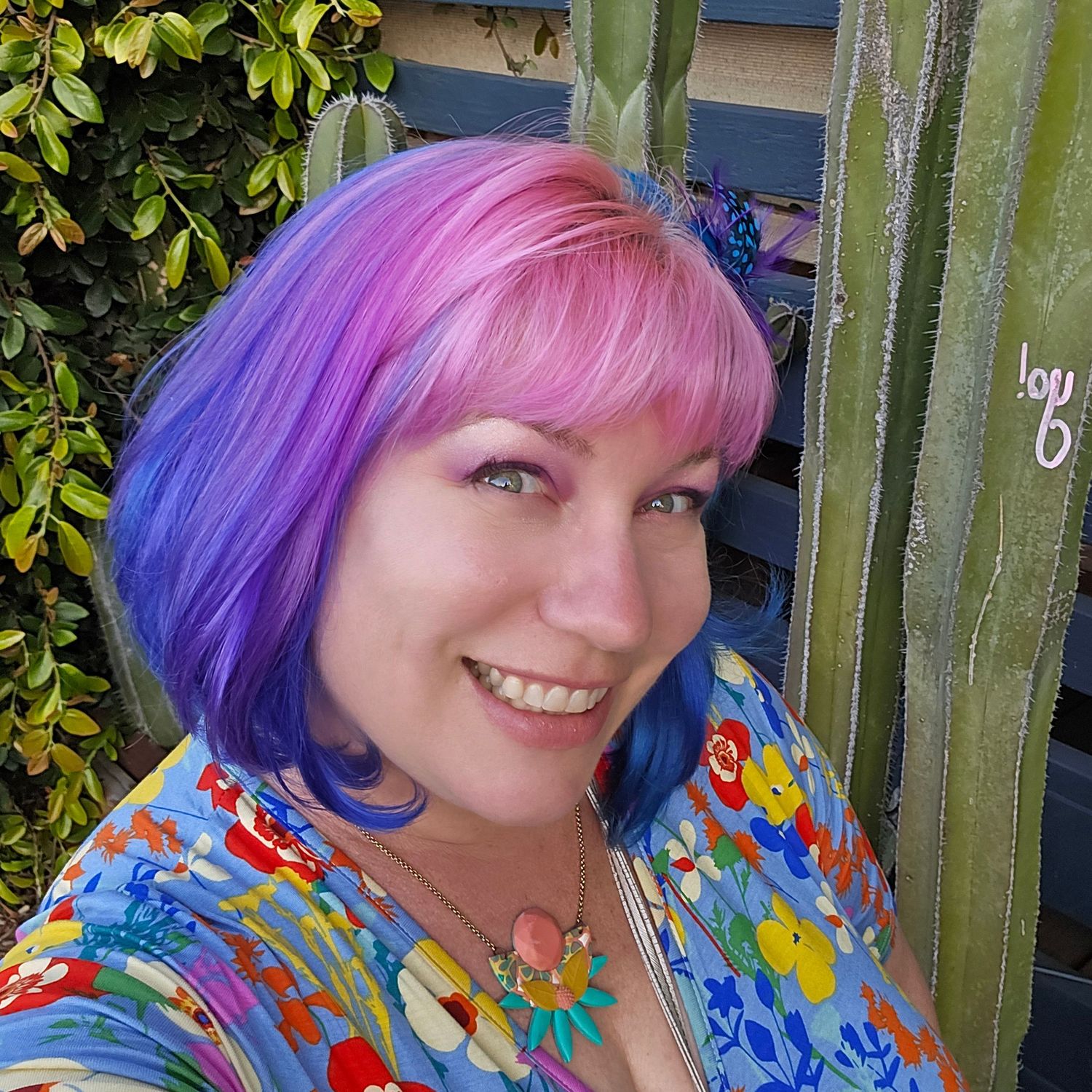 Colorful self portraits with vibrant purple and pink hair against garden fence.