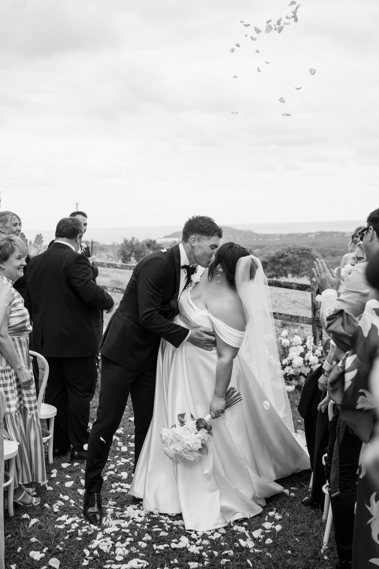 Black and white photograph of wedding guests in formal attire gathering outdoors on a hillside during a celebration.