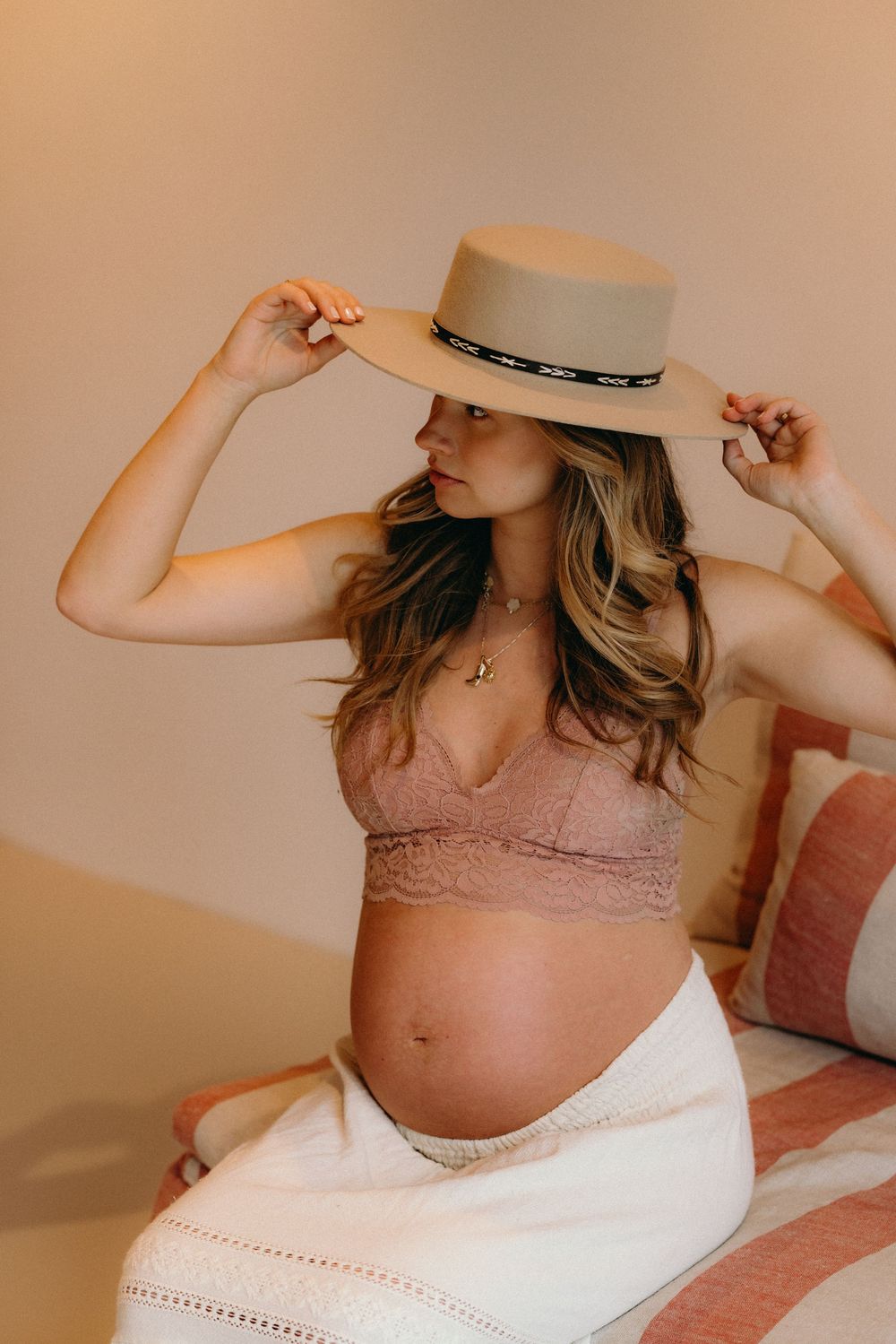Person wearing wide-brim hat and pink lace top during indoor maternity photoshoot.