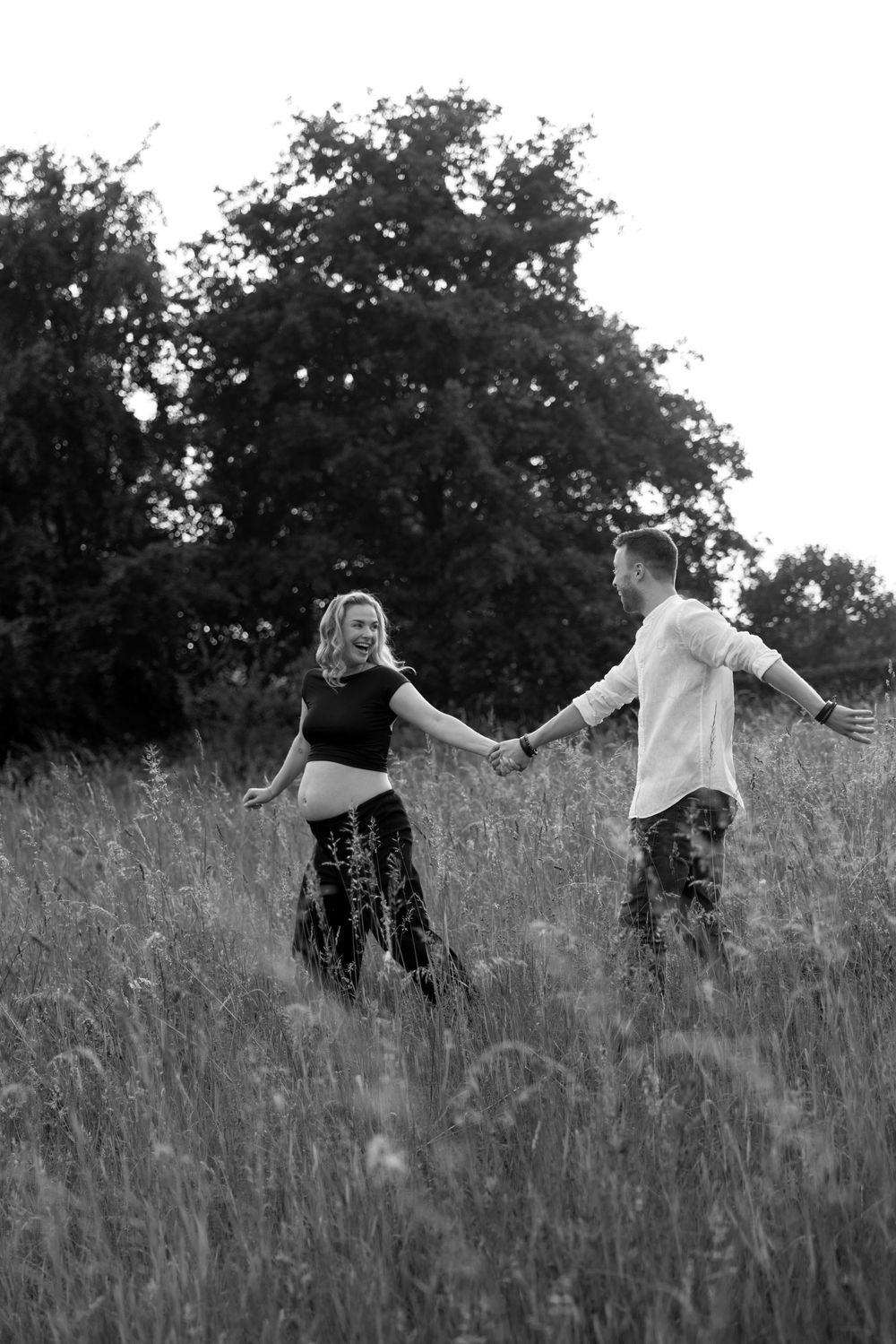 Two people dance joyfully through a meadow with arms outstretched.