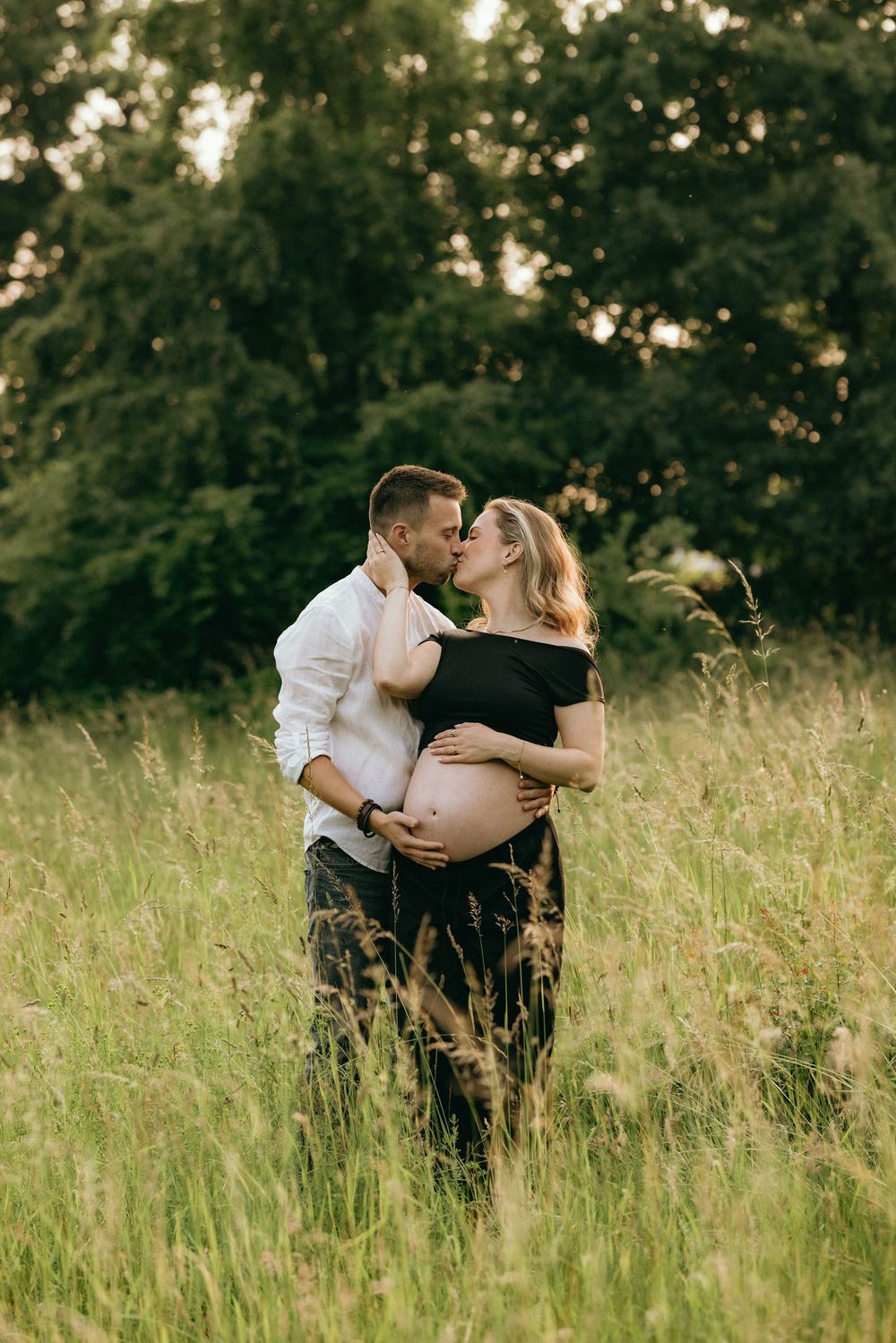 A romantic maternity photo of a couple embracing in a sunlit meadow.