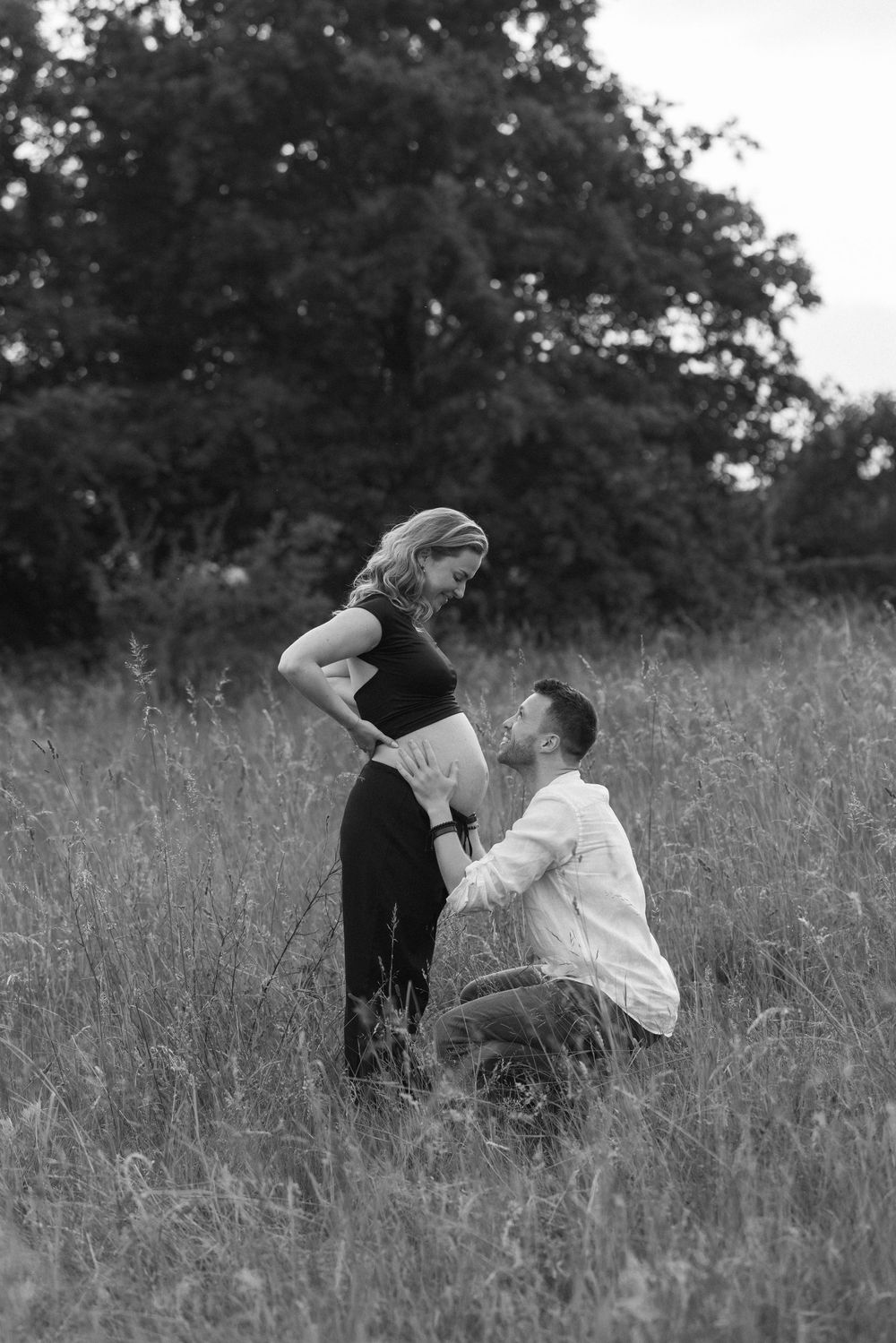Black and white photo of a couple sharing tender moments in a grassy field.