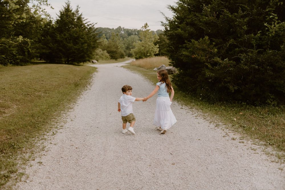 Two people dancing together on gravel path surrounded by green trees.