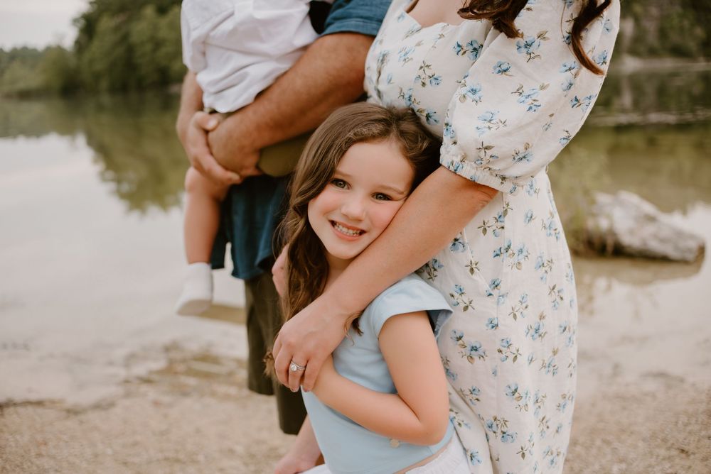 Child hugging parent by lakeside during family photoshoot.