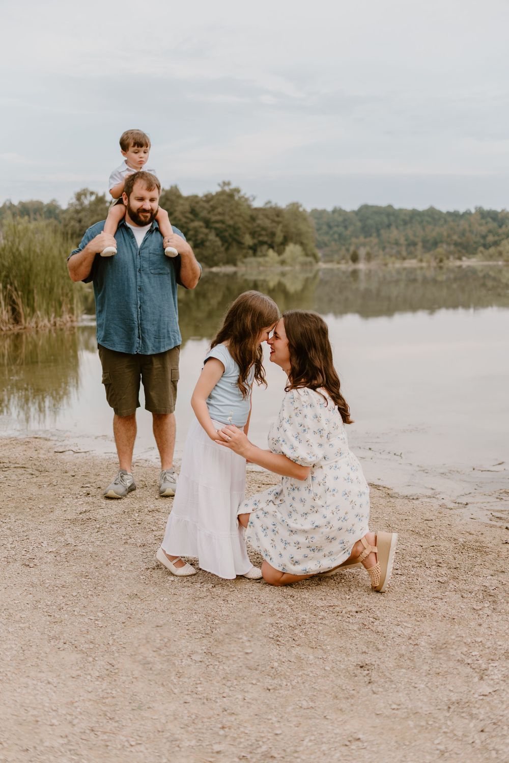 A family shares a tender moment together by a serene lake with tall reeds in the background.