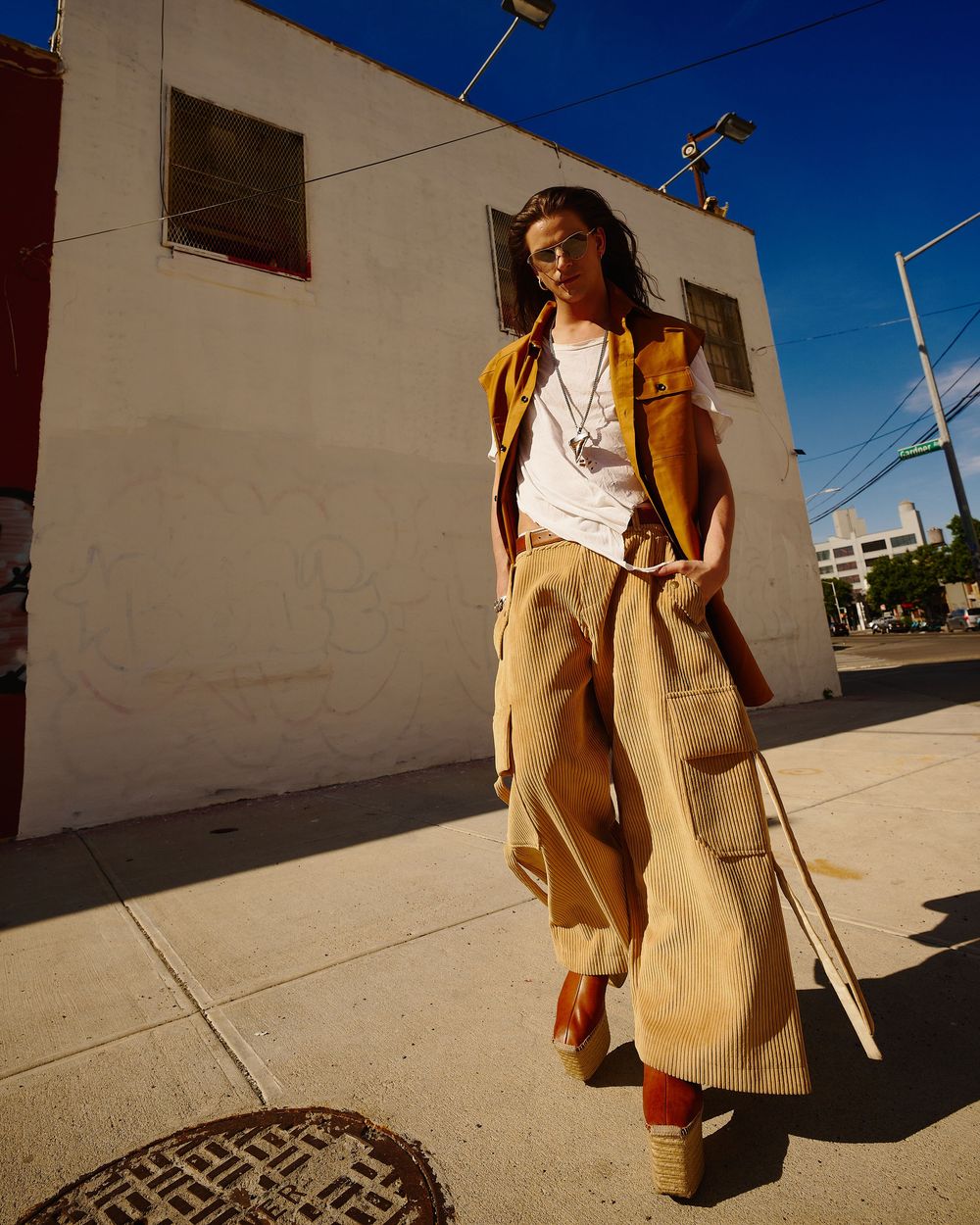 Person in a tan sweater vest and white shirt walking through urban environment in dramatic low-angle lighting.