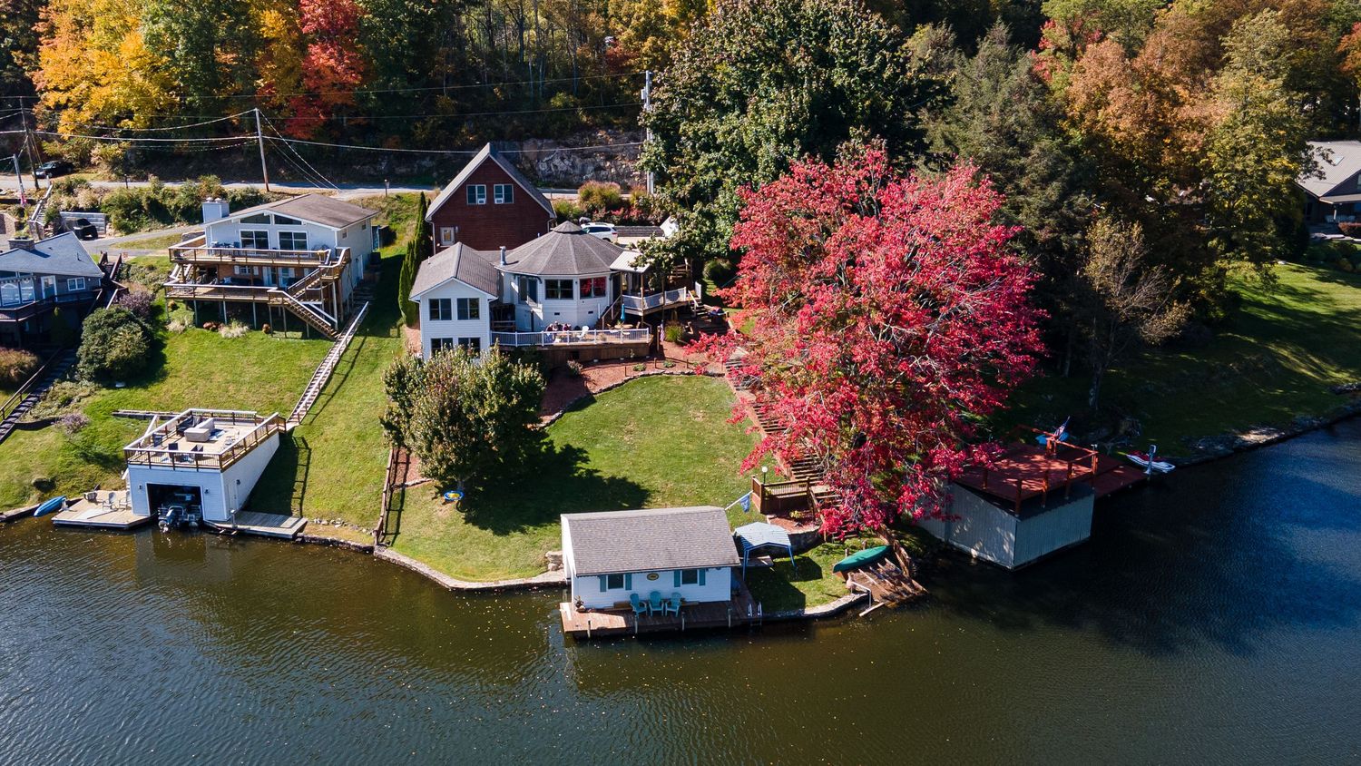 Aerial panoramic view of lakefront homes with vibrant autumn foliage and docks along the shoreline.