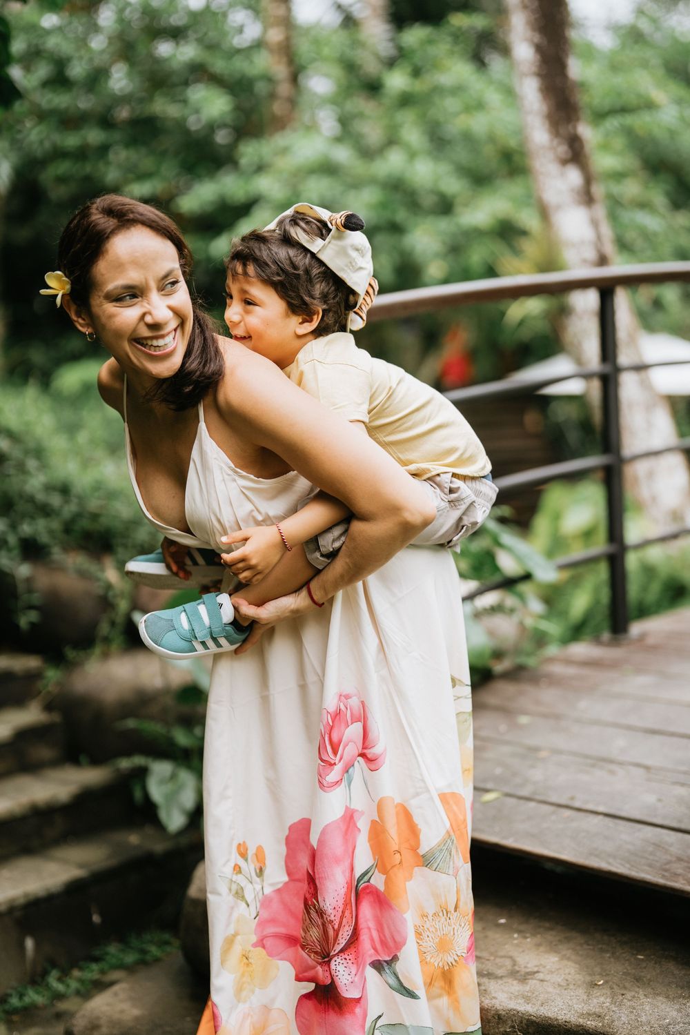 Two people share joyful moments on a wooden walkway surrounded by tropical greenery.
