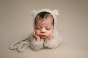Sleeping newborn baby rests peacefully wearing a white wrap against a neutral beige background.