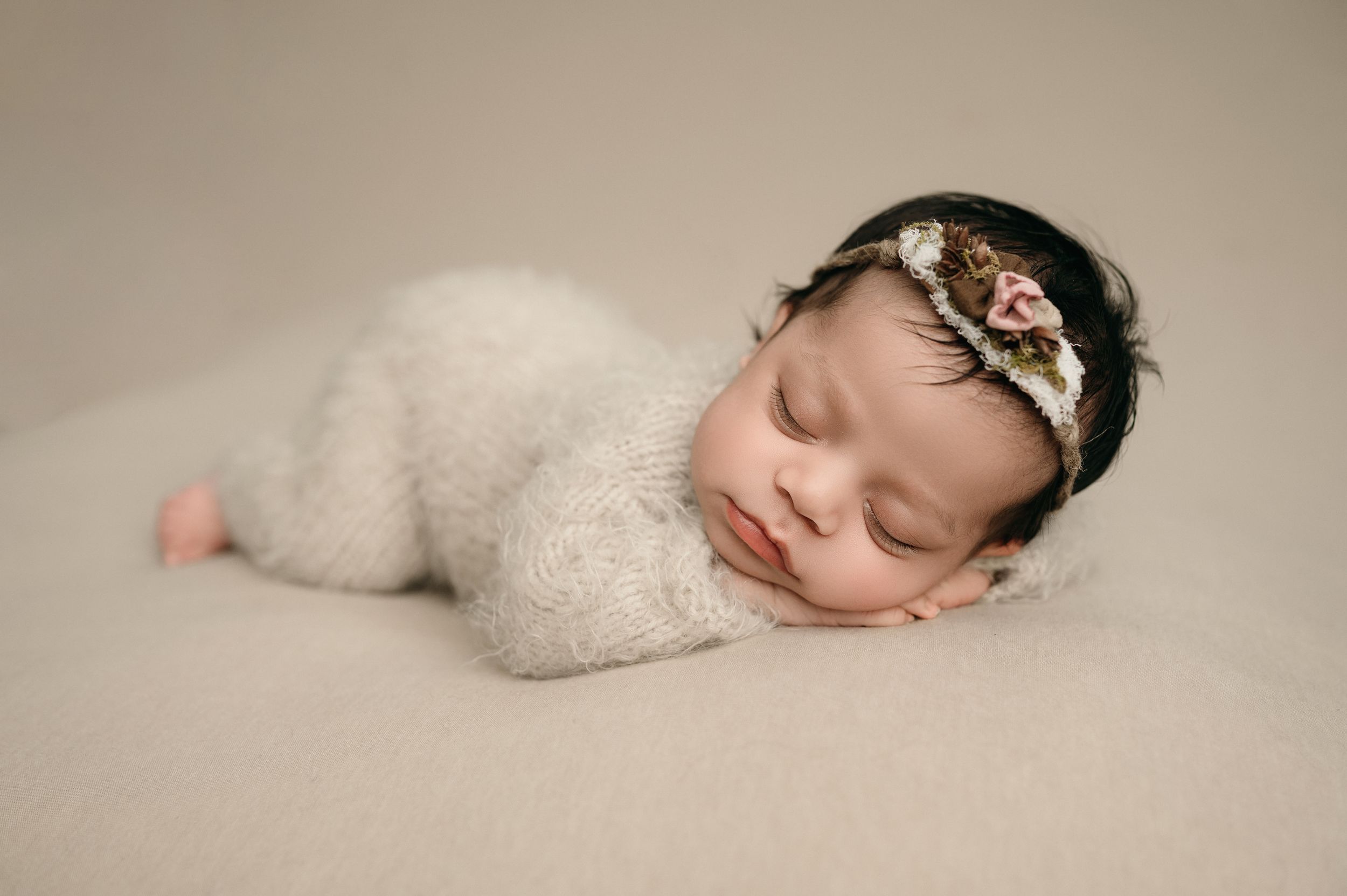 Peaceful newborn baby wearing a delicate lace headband sleeps soundly on soft white fabric during professional photo session.