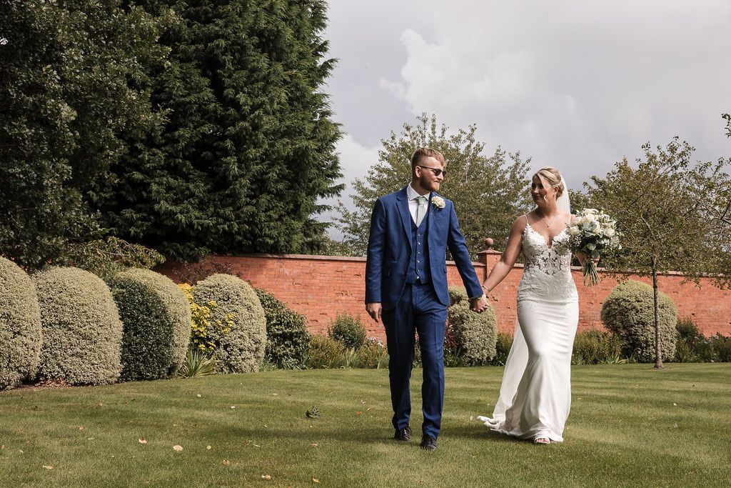 Bride and groom holding hands while walking across the lawn at Kelham House