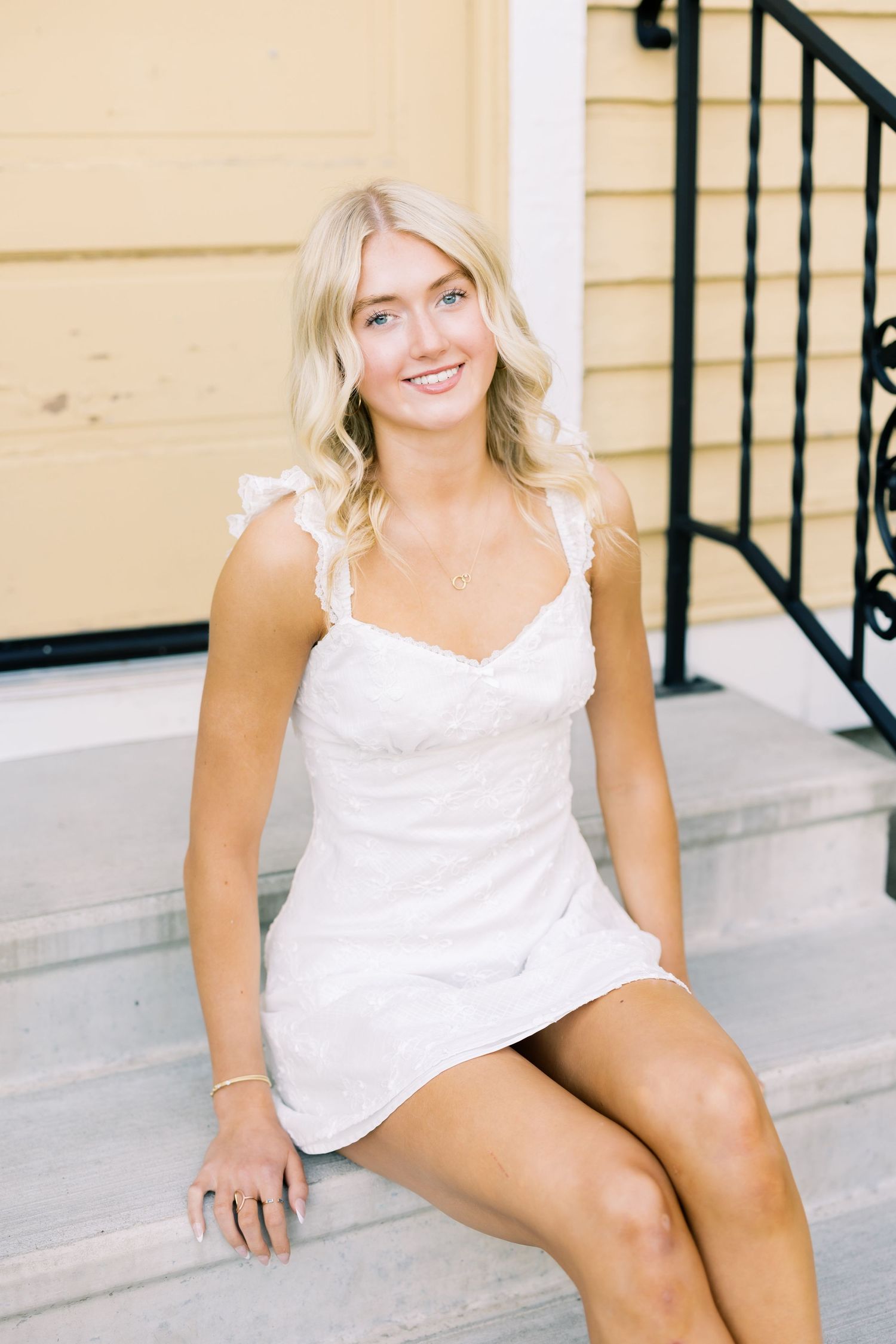 A woman in a white summer dress sits casually on outdoor concrete steps.