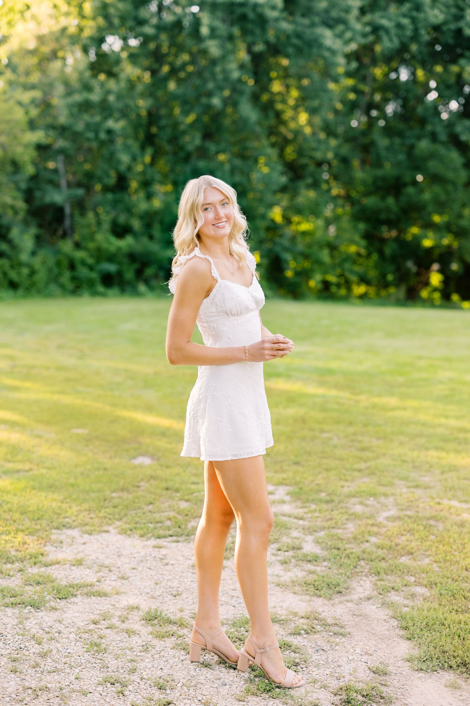 A white lace sundress ensemble photographed in a sunny outdoor setting among green grass and trees.