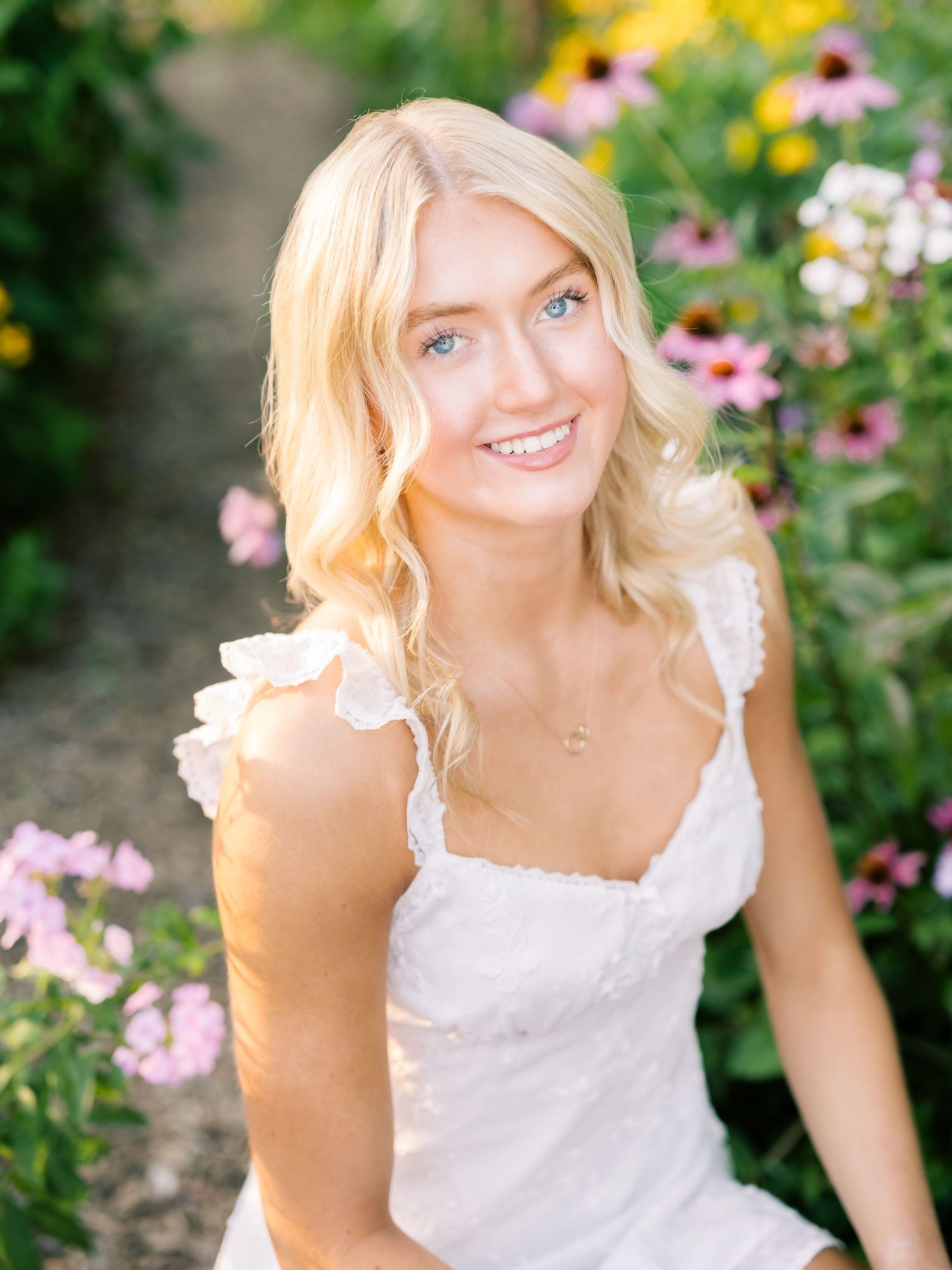 Outdoor portrait with colorful flower garden backdrop and white lace dress.
