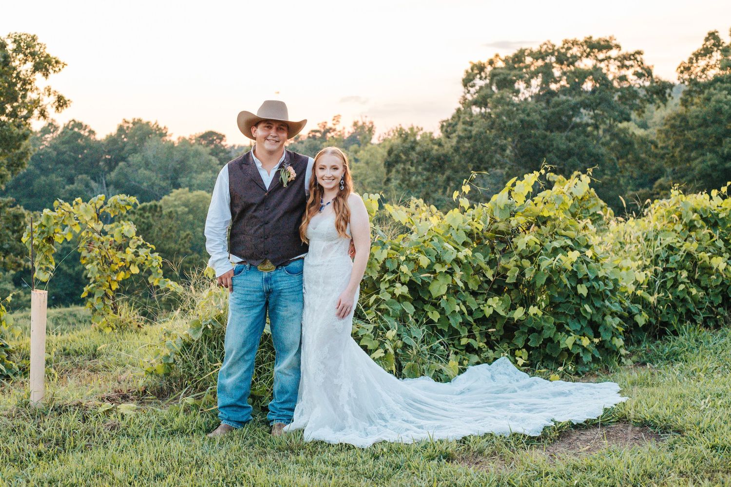 A western-themed wedding couple poses together in a scenic vineyard.