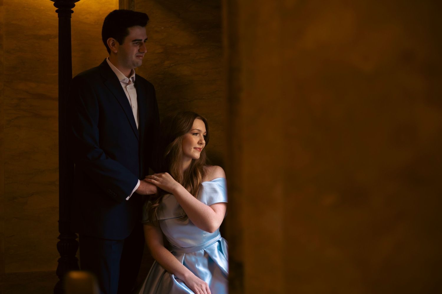A wedding couple dancing together in an elegant low-lit ballroom setting with moody golden lighting.