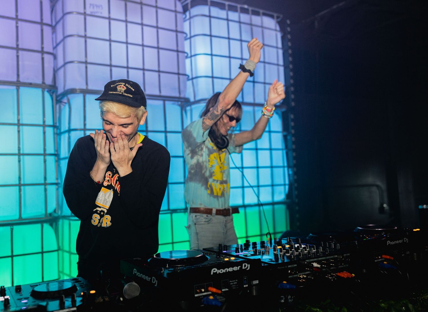 DJ performing at a nightclub with colorful blue and green lighting effects in the background.