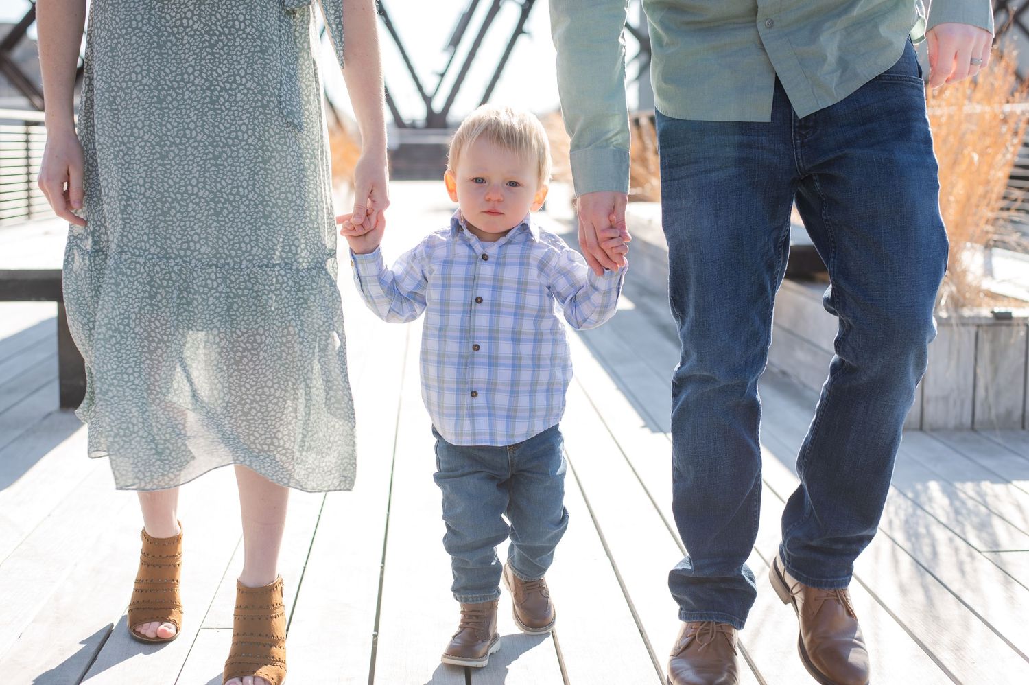 A row of feet and legs in different shoes and styles stand together on a wooden deck outdoors.