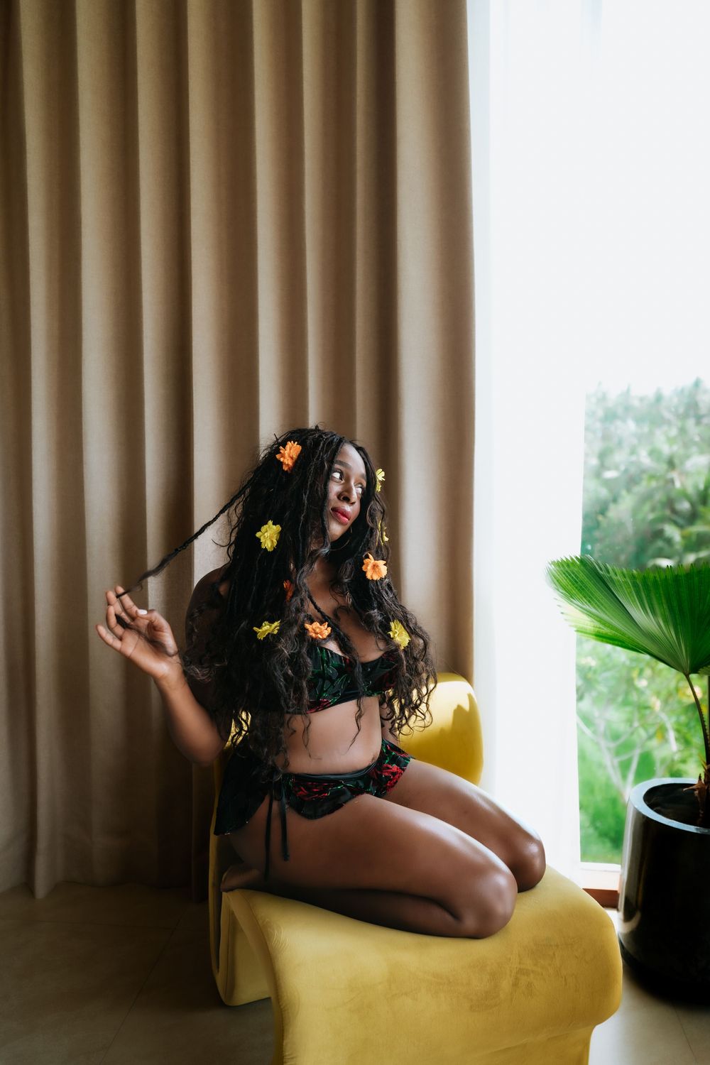 Intimate portrait on yellow chair with flowers in hair and draped curtains.