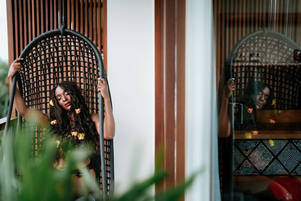 Relaxed pose in hanging rattan chair with tropical decor and plants.