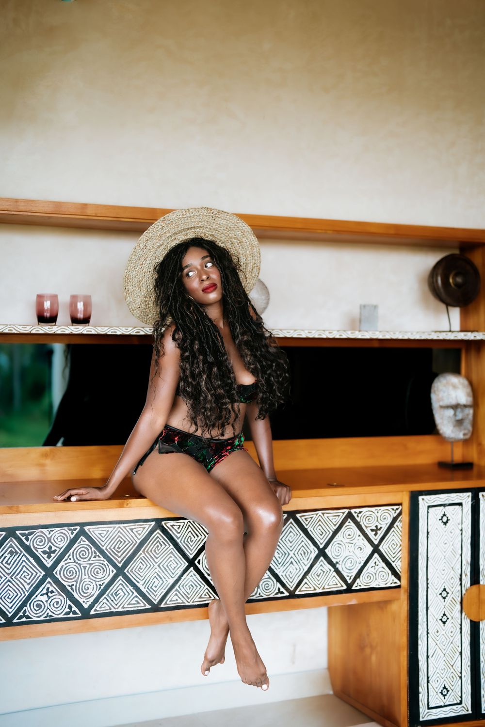 Artistic portrait featuring a straw hat against decorative geometric wall patterns.