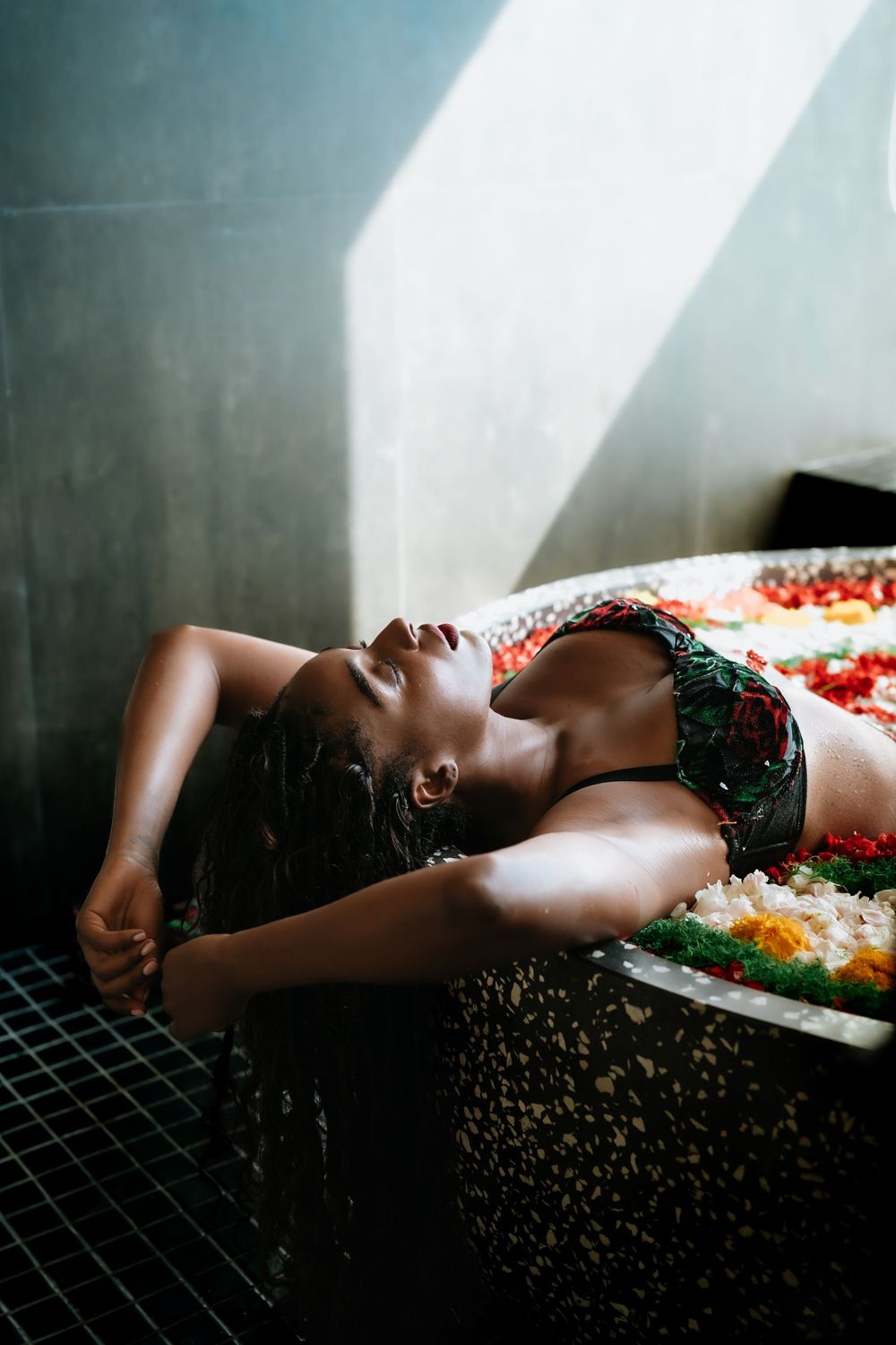 Dramatic boudoir photography with flowers and natural light creating artistic shadows.