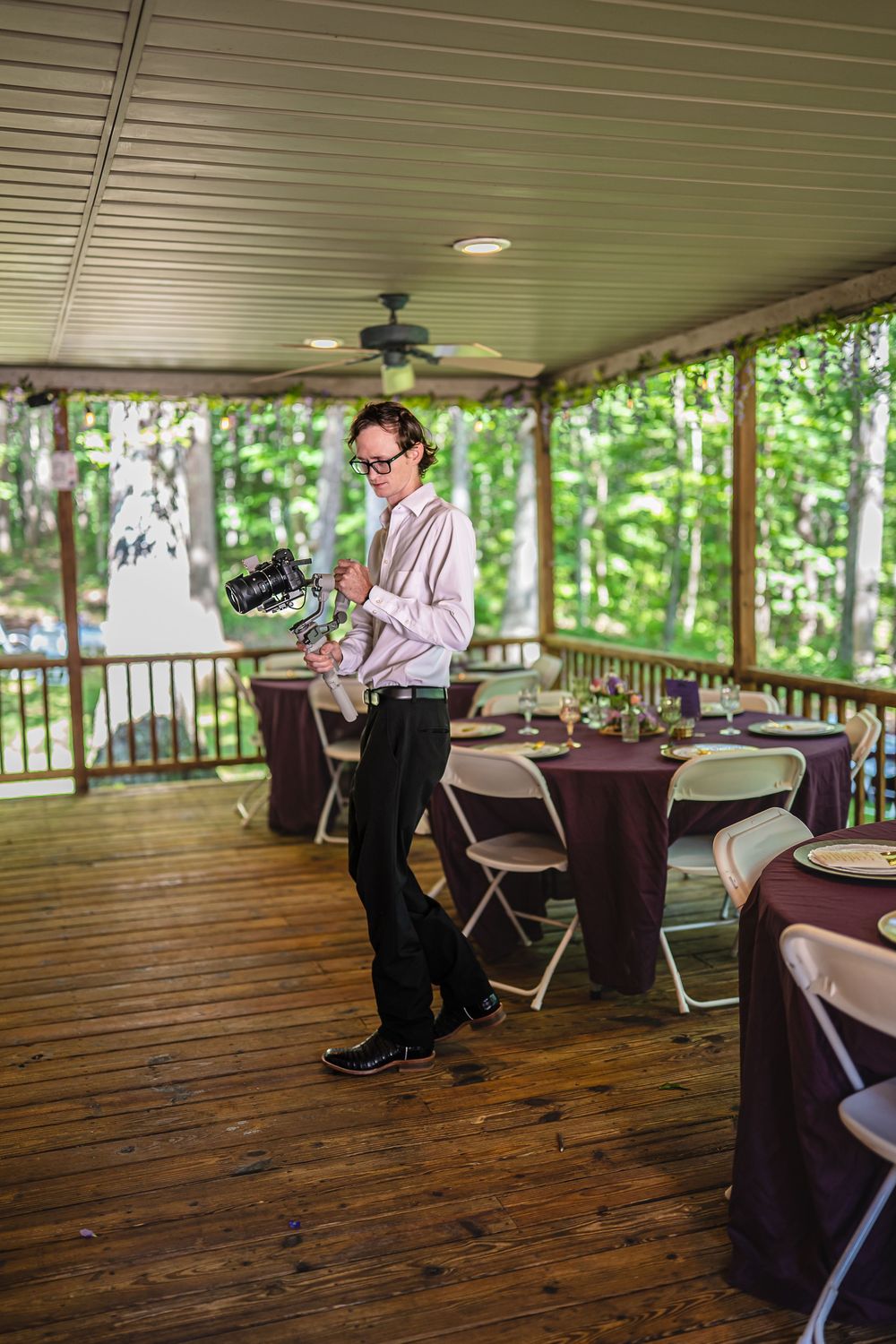Musicians performing at an outdoor covered venue with wooden floors and round tables set up for dining or events.
