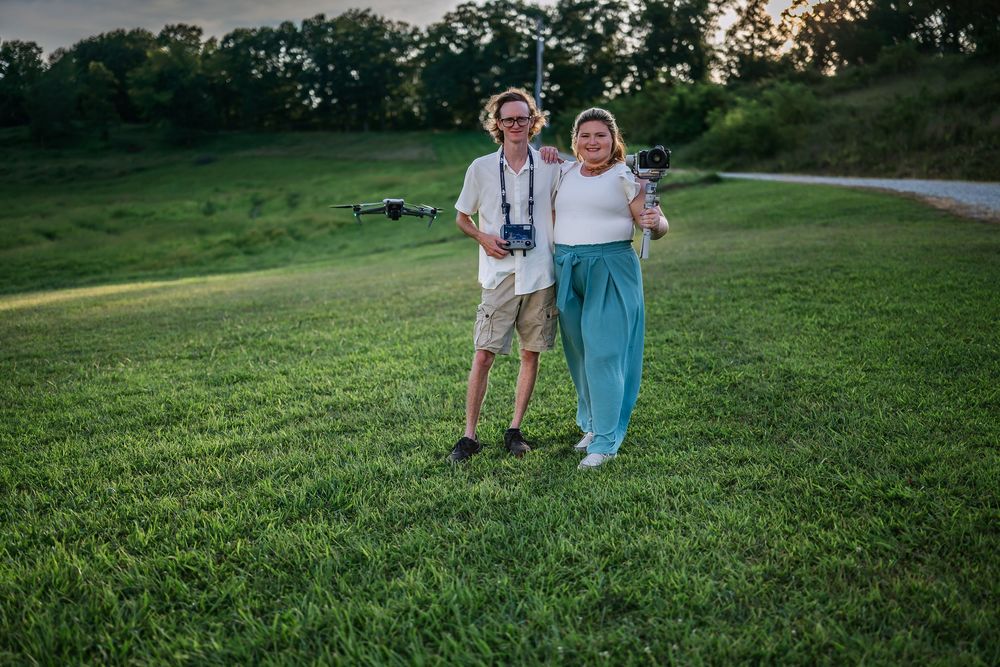 Couple walking hand in hand across a lush green hillside at sunset on a summer evening.