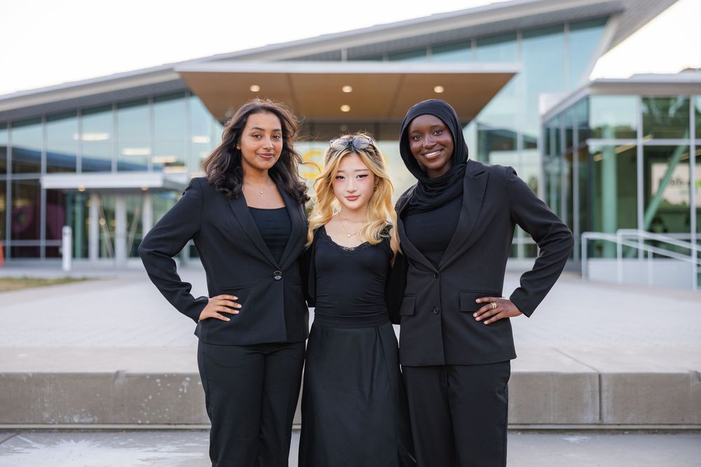 Three girls posed together in black professional outfits in front of the Siebel Center of Design