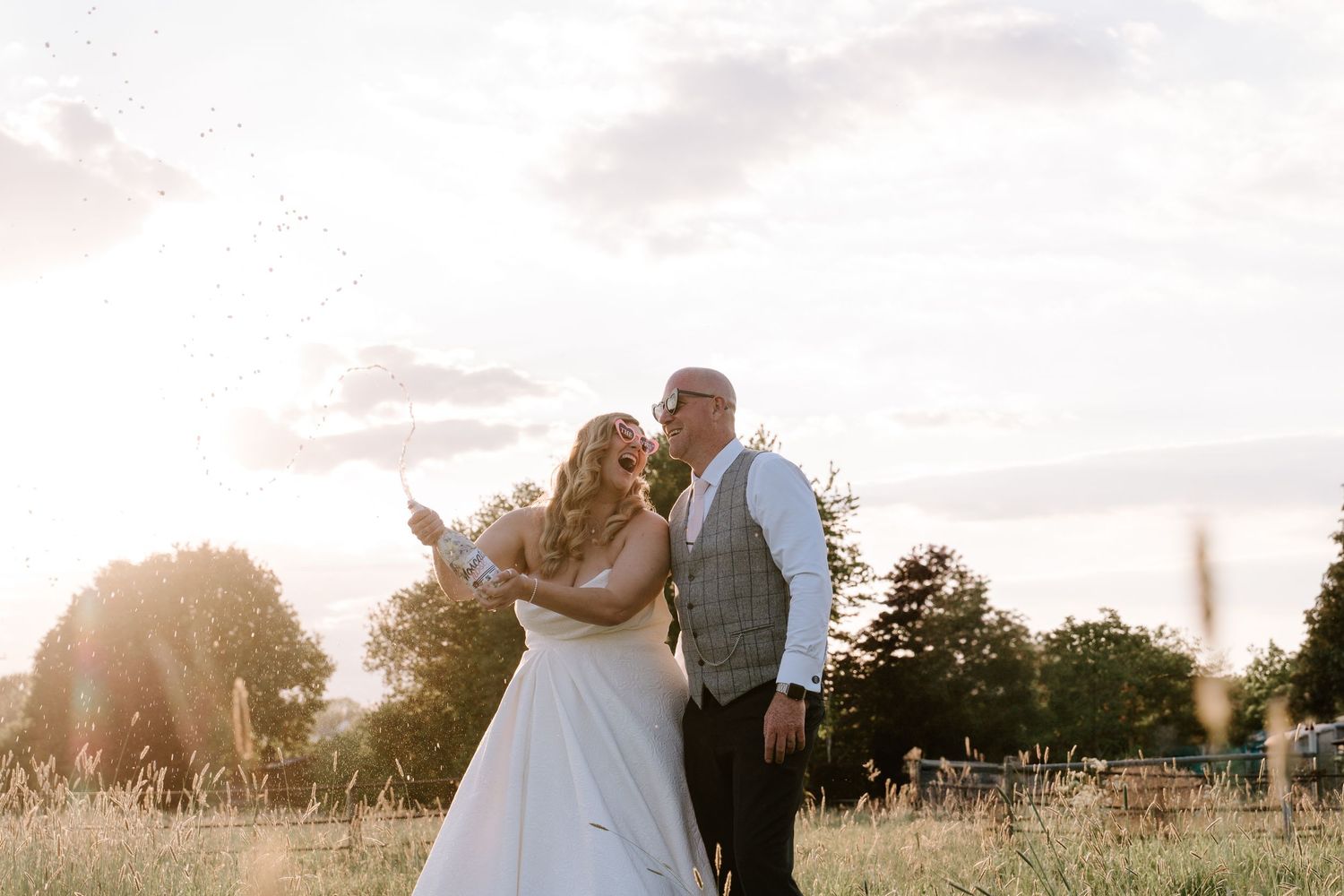 A romantic wedding couple shares candid moments under a graceful weeping willow tree on a lush green lawn.
