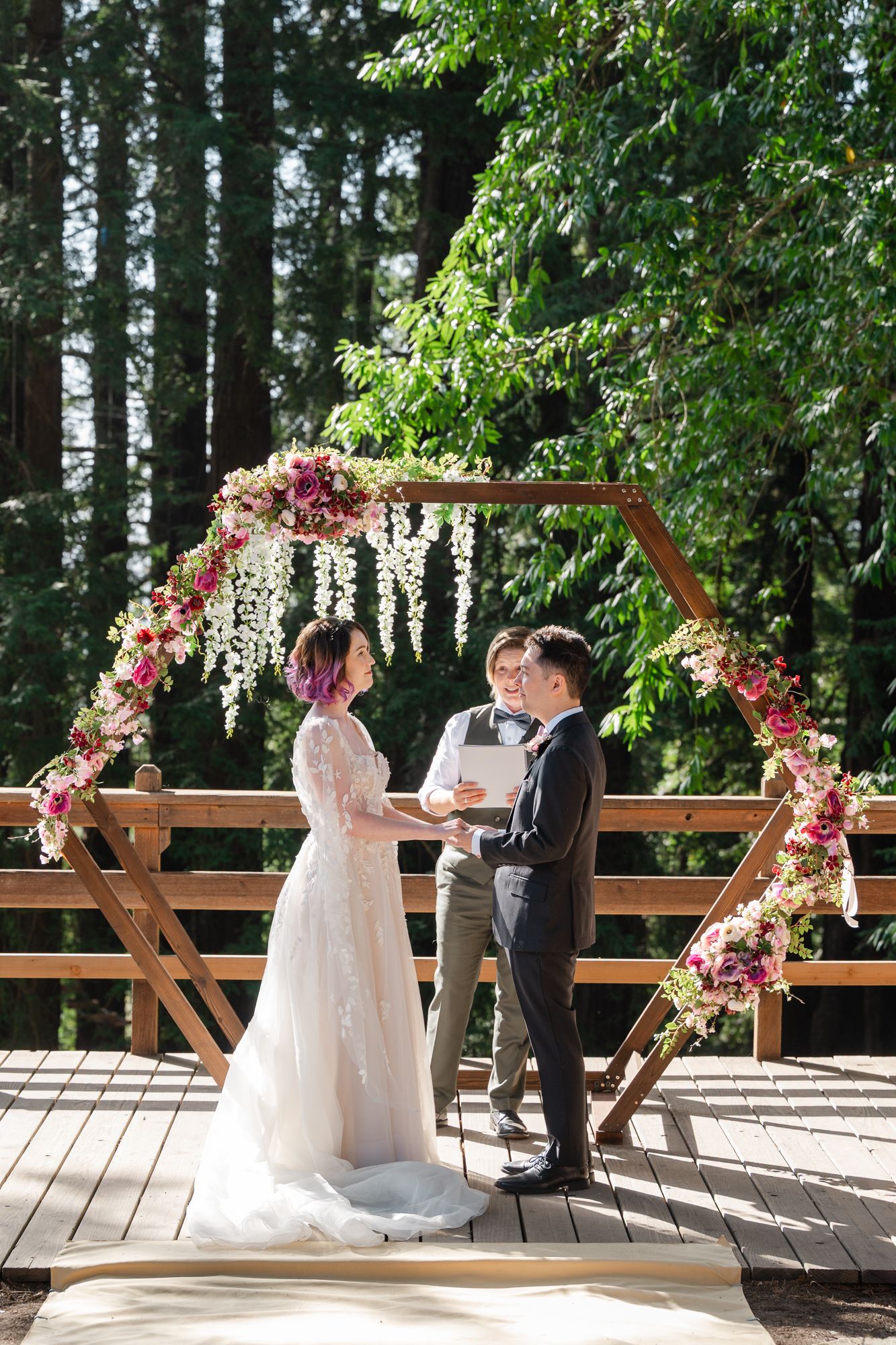 A decorated outdoor wedding ceremony venue with wooden railings and a floral arch during a summer celebration.