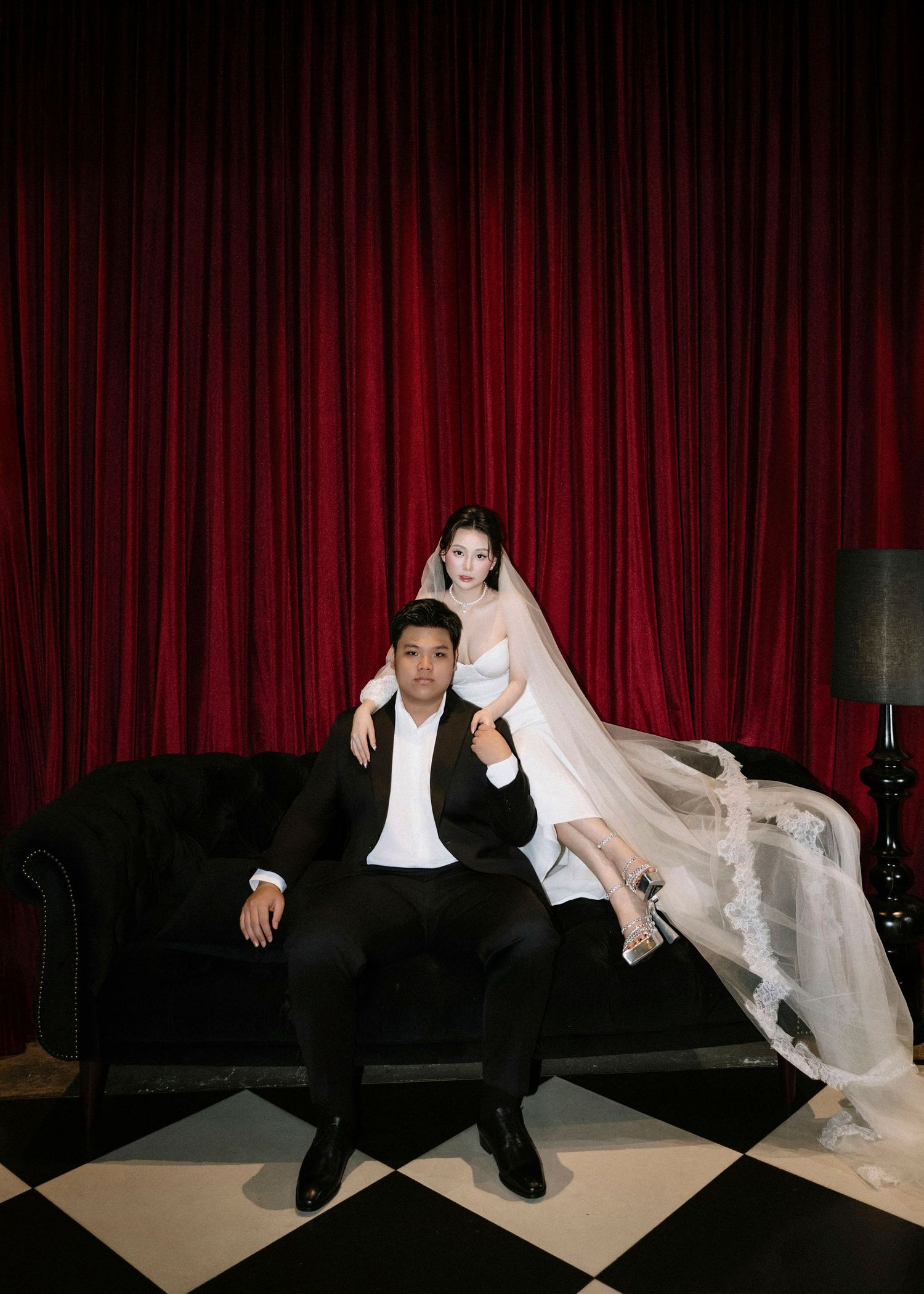 Asian wedding couple posing on black velvet sofa with bride in white gown and groom in black suit.