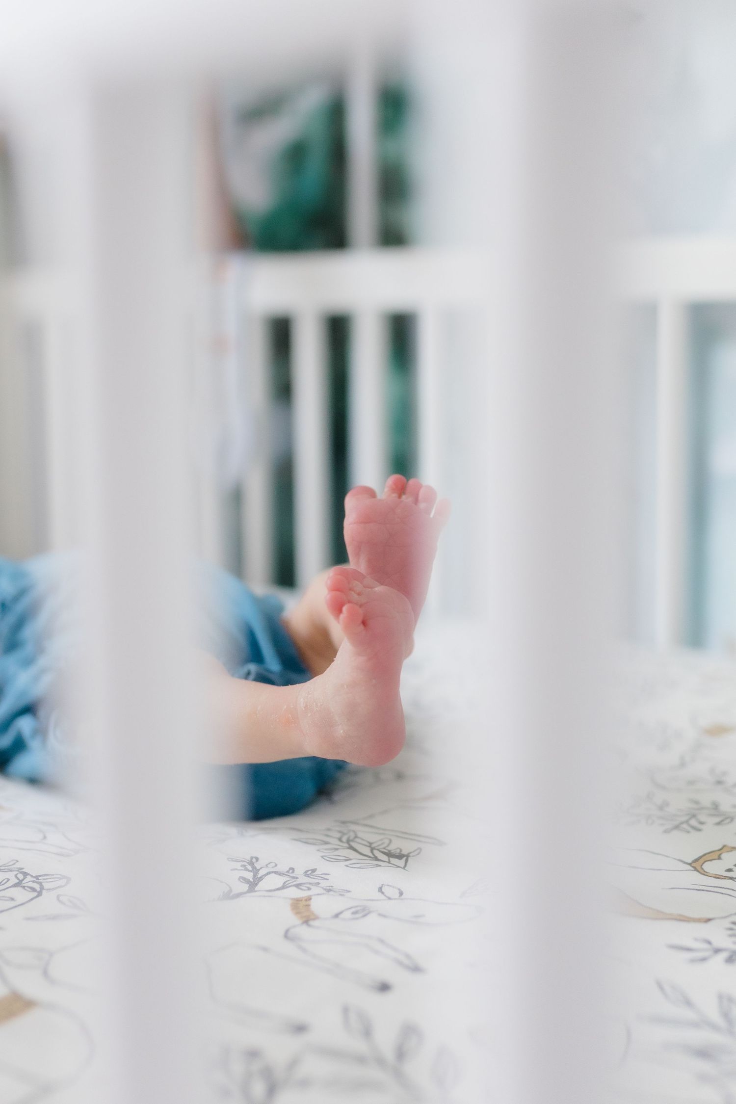Tiny baby feet viewed through white crib slats against floral bedding.