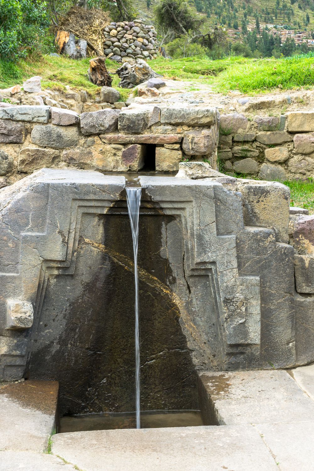 Ancient stone fountains with water spouts carved into stone walls at a historic archaeological site in Peru.